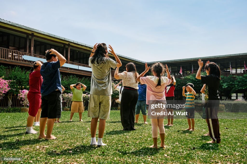 Joyful children playing in circle with teacher at school playground