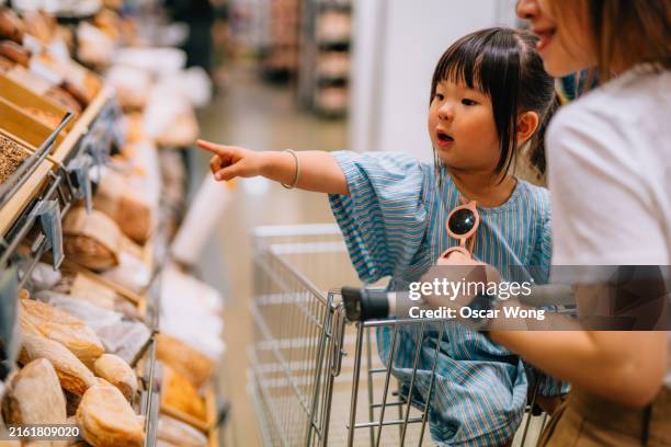 young asian mother and her little girl picking bread in bakery section of supermarket - curiosity shop stock pictures, royalty-free photos & images