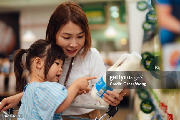 young asian mother and daughter reading nutrition label on milk bottle while shopping in supermarket - food allergy stock pictures, royalty-free photos & images