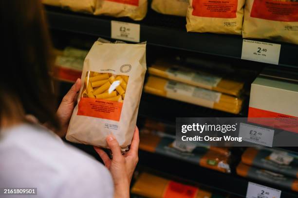 young woman looking at nutrition label of a package of pasta from the shelf in supermarket - product advertisement stock pictures, royalty-free photos & images