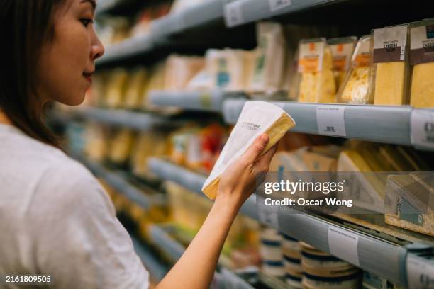 young asian woman looking at nutrition label of a slice of cheese in supermarket - cheese stock pictures, royalty-free photos & images