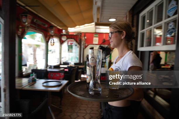 July 2024, Spain, Palma: Noemie brings customers their orders at the Zur Krone restaurant on Arenal beach. Photo: Clara Margais/dpa