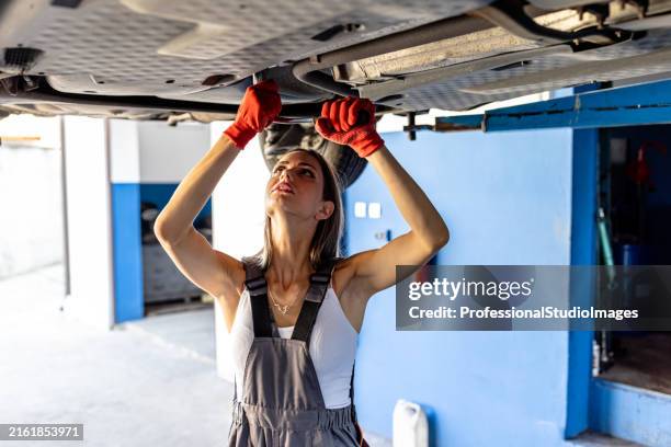 a female auto mechanic is fixing exhaust system under the lifted car. - skiftnyckel bildbanksfoton och bilder
