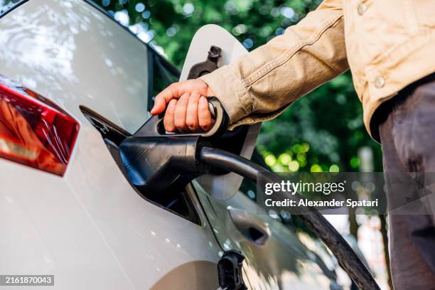 man's hand plugging in a charging lead to the electric car - hybrid car stock pictures, royalty-free photos & images