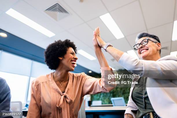 compañeros de trabajo chocando los cinco en la oficina - choque de manos en el aire fotografías e imágenes de stock