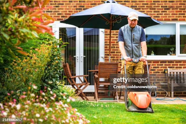 mid adult male home owner mowing lawn in the back yard of his house - lawn stock pictures, royalty-free photos & images