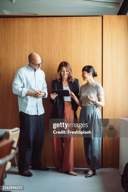 collègues discutant du travail sur tablette dans un environnement de bureau moderne - trois personnes photos et images de collection