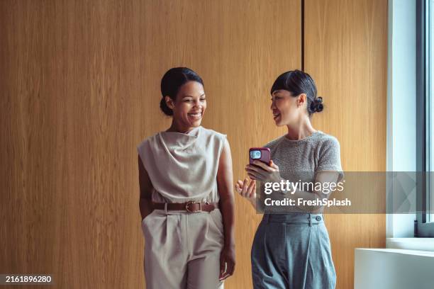 businesswomen engaging in friendly conversation with smartphone - bedrijfscultuur stockfoto's en -beelden