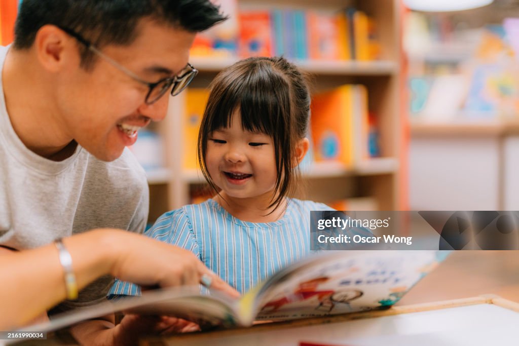 Young Asian Father having fun reading with his little daughter in bookshop