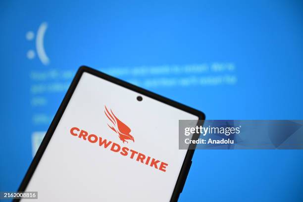In this photo illustration, the CrowdStrike logo on phone screen is displayed in front of Blue Screen of Death errors on laptop screen in Ankara,...