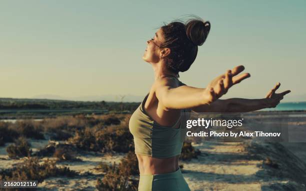 young pretty woman standing outdoors enjoy moment of freedom with outstretched arms feel happy and satisfied, sea and coastline on background. life, moments concept - calções imagens e fotografias de stock