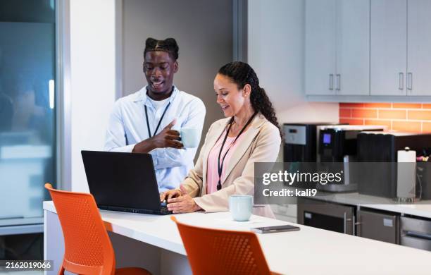 two office workers using laptop in kitchenette - kitchenette stock pictures, royalty-free photos & images