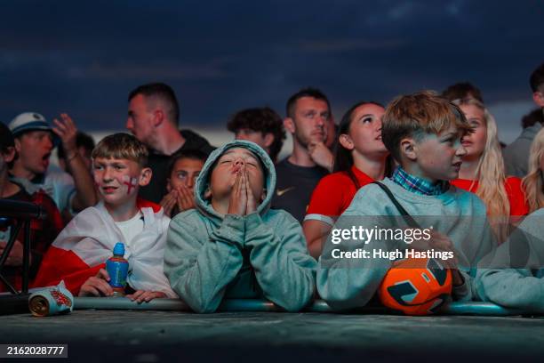 Young England football fans react as they watch the match on a giant screen on the beach at the Watering Hole, as England face Spain in the Men's...