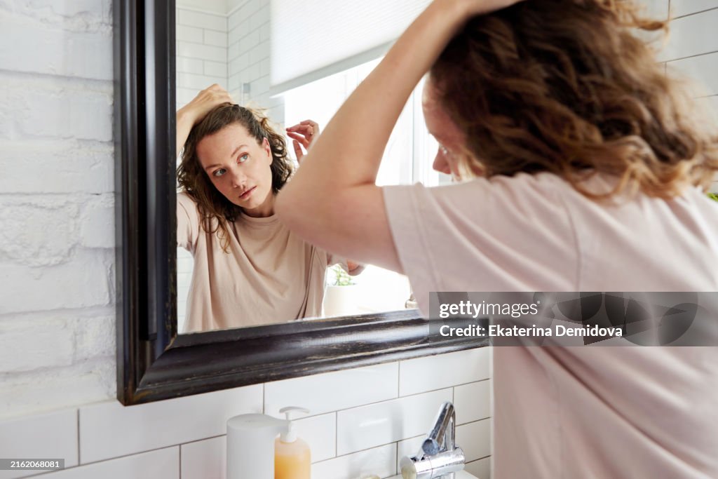 A young person styling their hair in front of a bathroom mirror, reflecting their youthful lifestyle