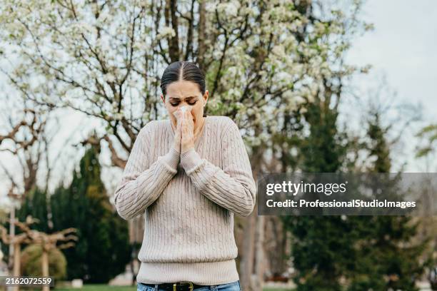 jeune femme éternuant avec des allergies dans un parc au printemps - éternuer photos et images de collection