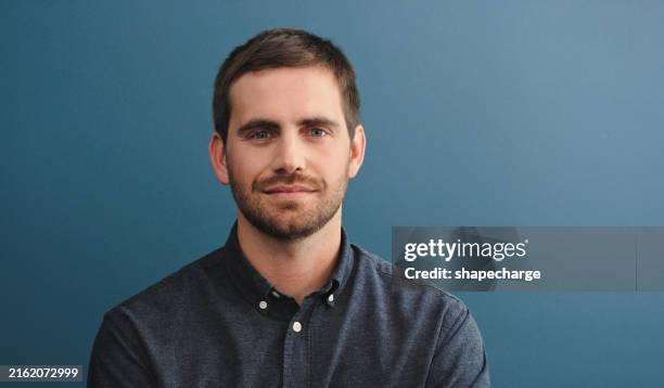 studio shot of a young man standing against a blue background - stoppelbaard stockfoto's en -beelden