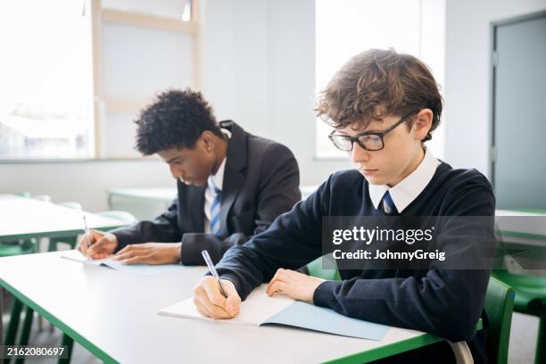 estudiantes masculinos enfocados escribiendo en cuadernillos de examen - uniforme de colegio fotografías e imágenes de stock