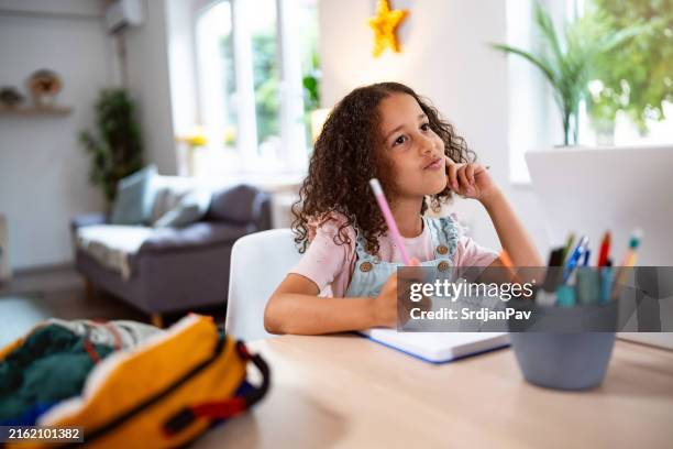 chica multirracial haciendo los deberes, en casa para la mesa del comedor - instrumento de escribir fotografías e imágenes de stock