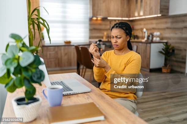 müde junge frau hat handgelenkschmerzen, während sie zu hause am laptop arbeitet - unbehaglich stock-fotos und bilder