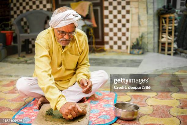 rural indian senior man grinding herbs on traditional stone grinder. - ayurveda stock pictures, royalty-free photos & images