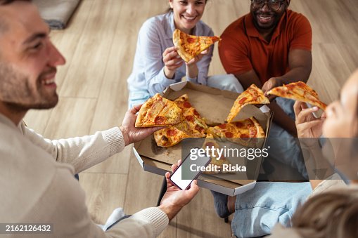 Friends enjoying pizza together at home with smartphone interaction - phone with white screen Friends enjoying pizza together at home with smartphone interaction - phone with white screen