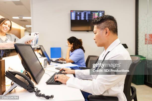 médico sério usa desktop no posto de enfermagem para trabalhar - registo-médico-eletrónico - fotografias e filmes do acervo
