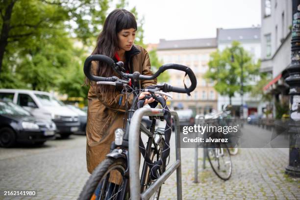junge frau, die ihr fahrrad auf der straße in der stadt abschließt - fahrradschloss stock-fotos und bilder