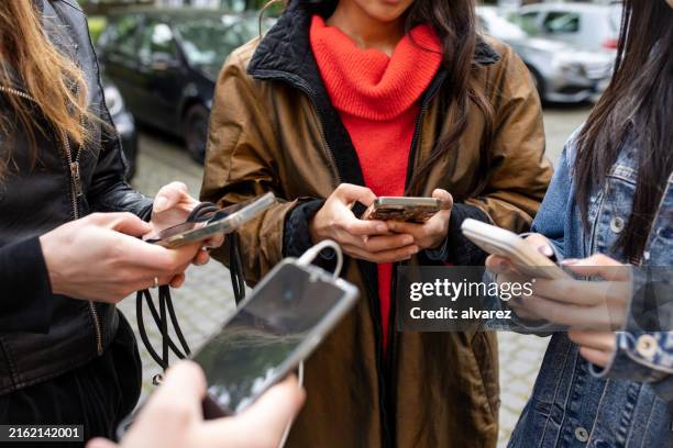 grupo de amigos que usan teléfonos inteligentes mientras están parados al aire libre en la ciudad - social media fotografías e imágenes de stock