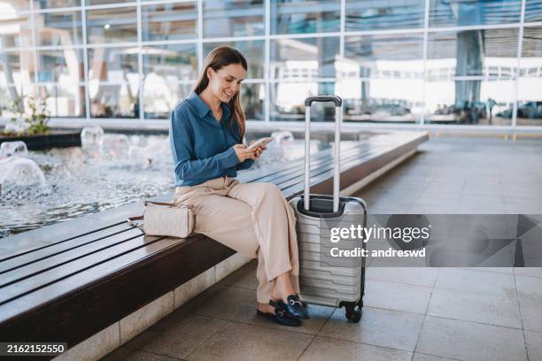 una mujer en el aeropuerto usando un teléfono inteligente - viaje de negocios fotografías e imágenes de stock