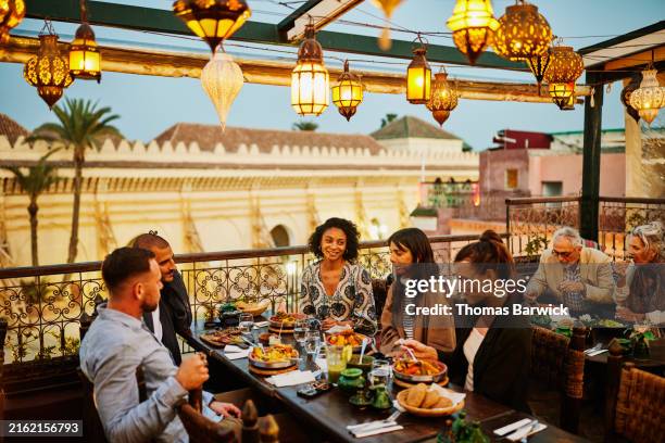 wide shot tourists laughing and eating tajine at restaurant - marrakech stockfoto's en -beelden