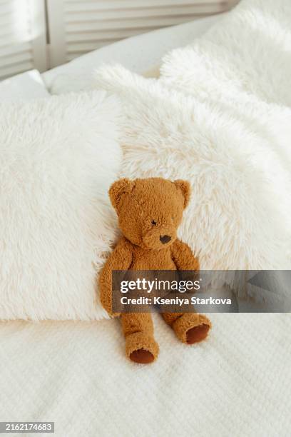 a brown teddy bear sits on a bed in a scandinavian-style bedroom near the window - doudou photos et images de collection