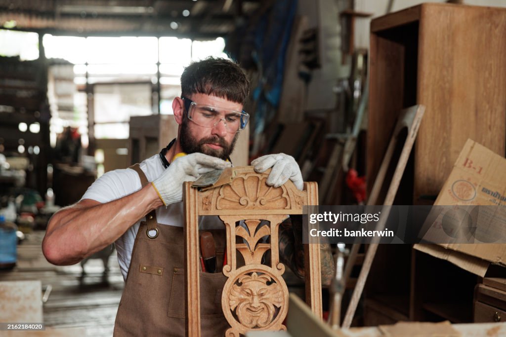 Young carpenter using sand paper clear scrap wood on the chair in factory