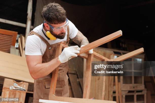 young carpenter clear scrap wood on the chair in factory - snickare bildbanksfoton och bilder