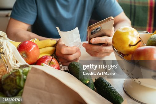 Senior man unpacking groceries at kitchen and looking at receipts, financial crisis, environment conservation and sustainability concept Senior man unpacking groceries at kitchen and looking at receipts, financial crisis, environment conservation and sustainability concept