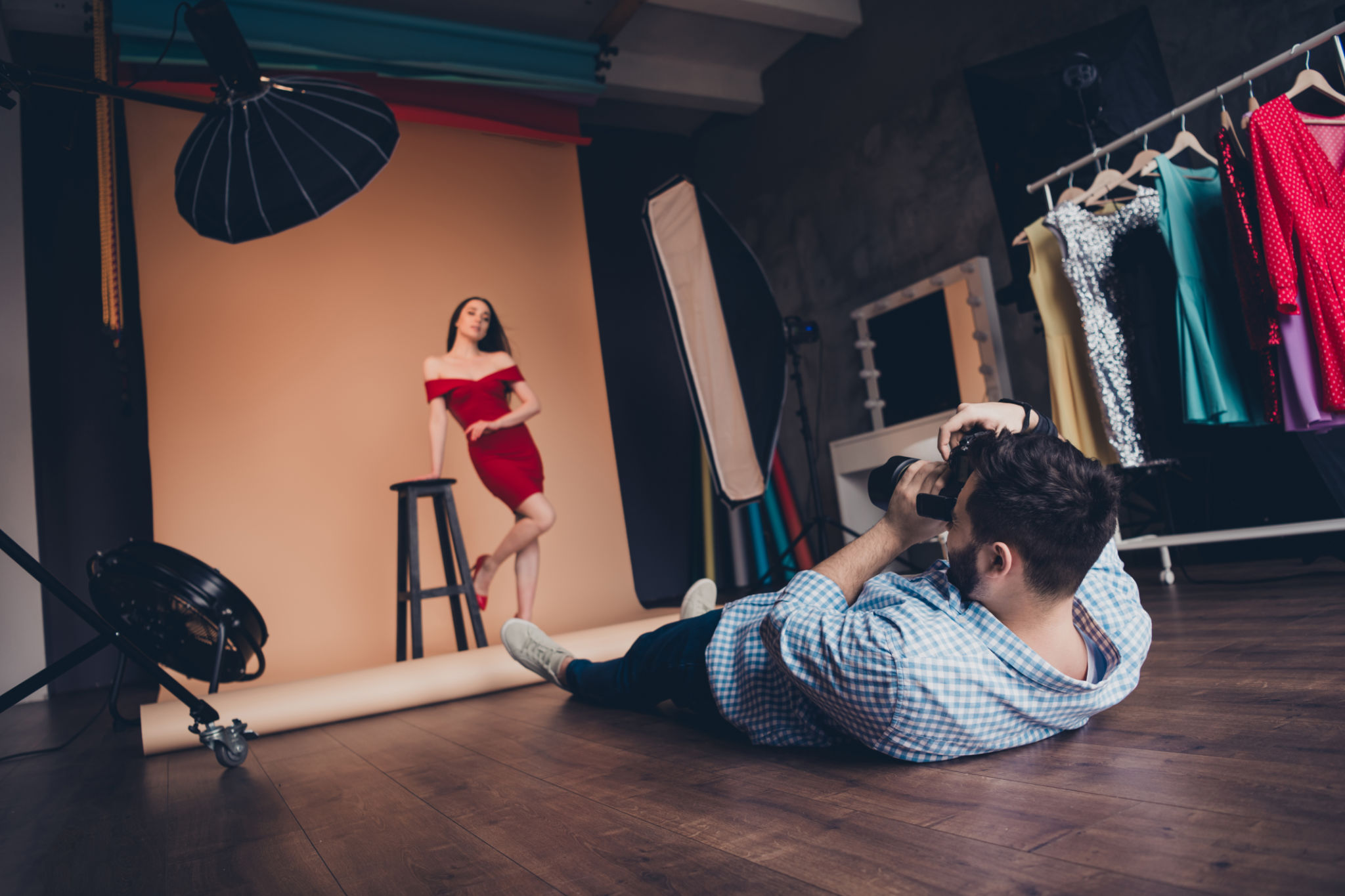 Fashion photographer lying and taking photo of beautiful female model posing in modern art studio indoors Fashion photographer lying and taking photo of beautiful female model posing in modern art studio indoors