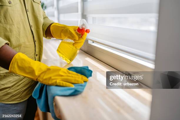 young man cleaning his window sill at home - schoonmaakmiddel stockfoto's en -beelden