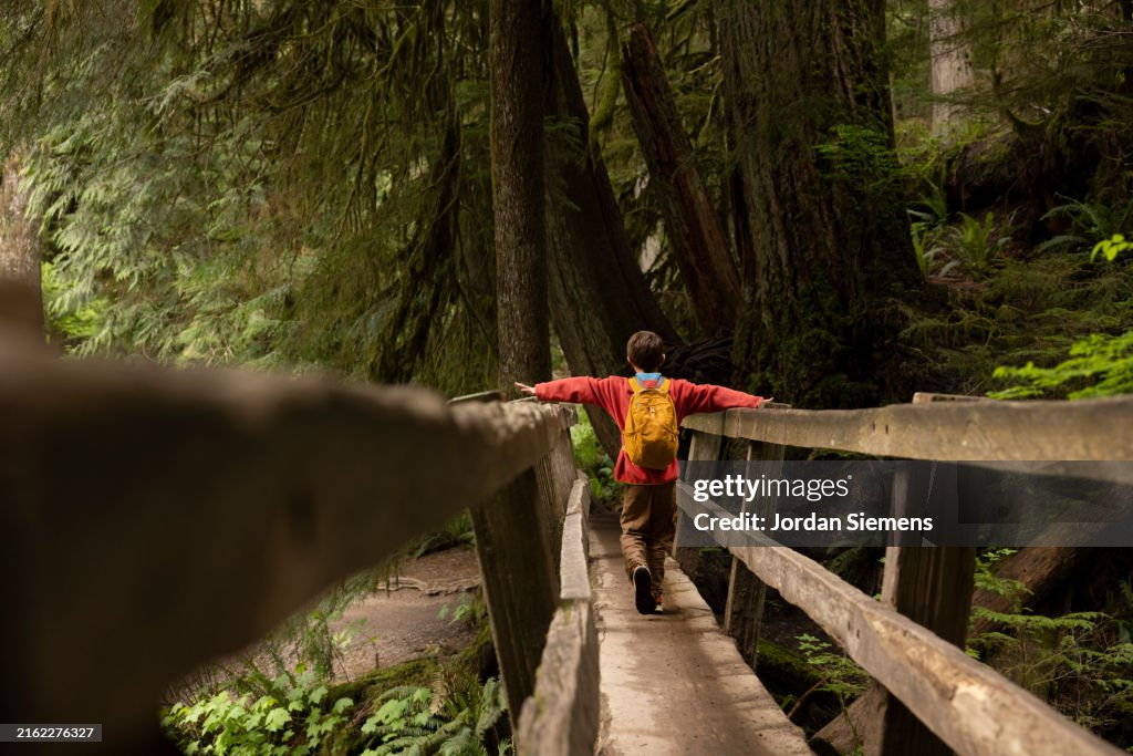 A young boy hiking across a wooden bridge.