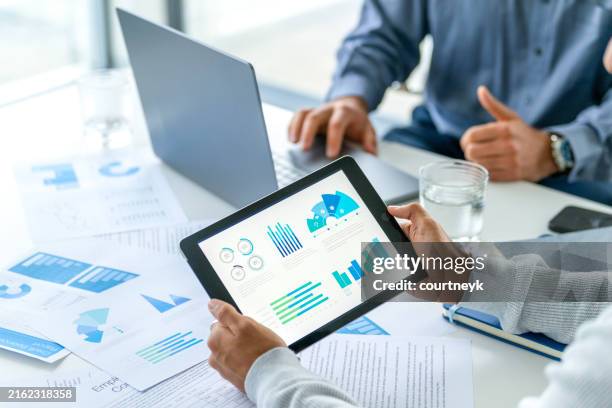 two business men meeting and looking at financial data, charts and graphs on a digital tablet and a laptop computer. - audit stock pictures, royalty-free photos & images