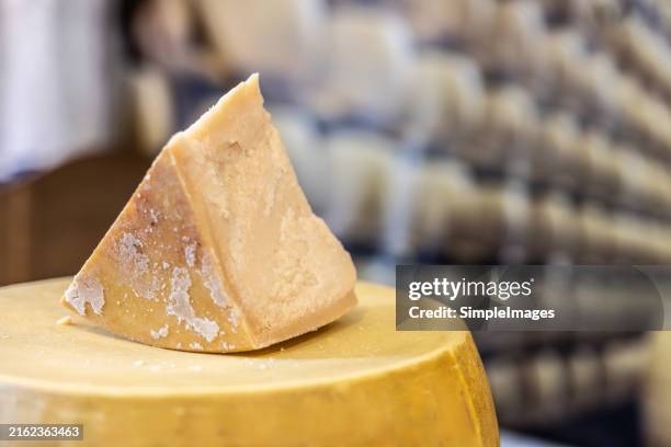 a loaf of parmesan cheese with a piece cut off in a cheese warehouse somewhere in italy. - hard cheese stock pictures, royalty-free photos & images