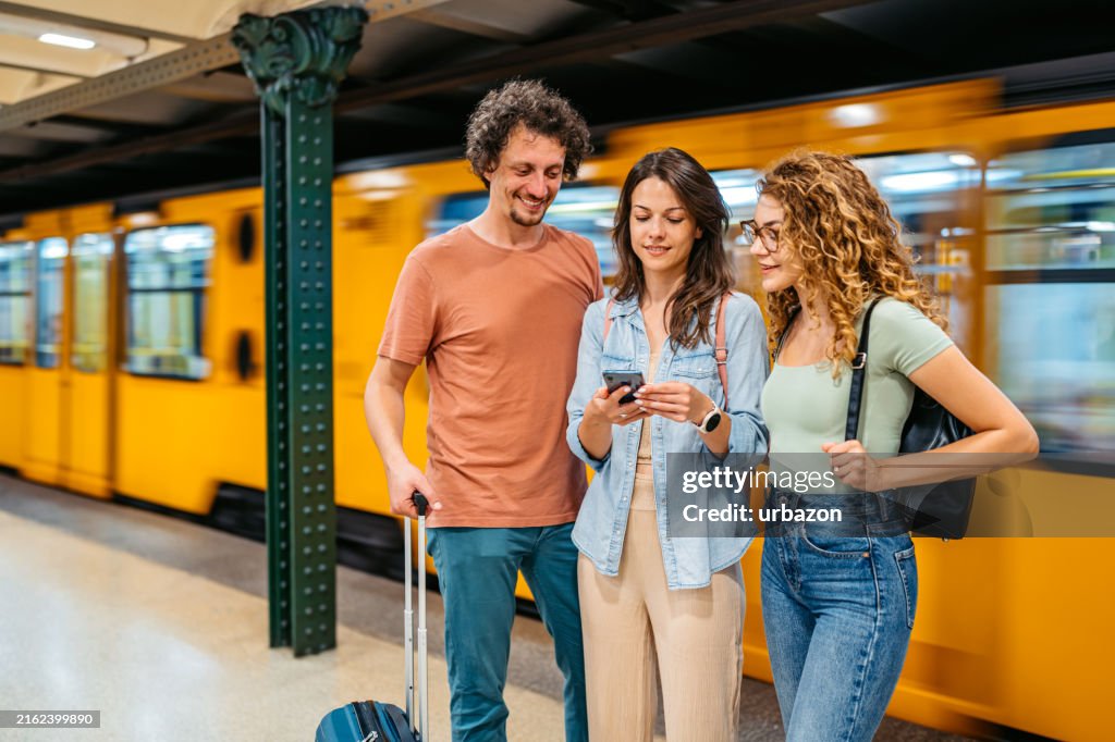 Three Friends Using A Phone While Waiting For A Subway Train In Budapest In Hungary