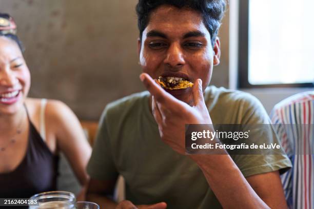 young man enjoying mexican food with friends in restaurant - nachos stockfoto's en -beelden