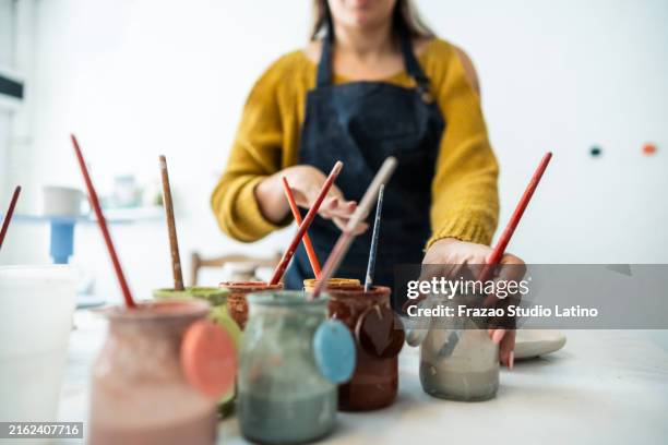 close-up of a woman picking up paints at ceramics workshop - ceramics stock pictures, royalty-free photos & images