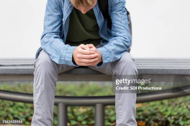 clasping his hands and looking down, teen boy makes decision - negatieve eigenwaarde stockfoto's en -beelden