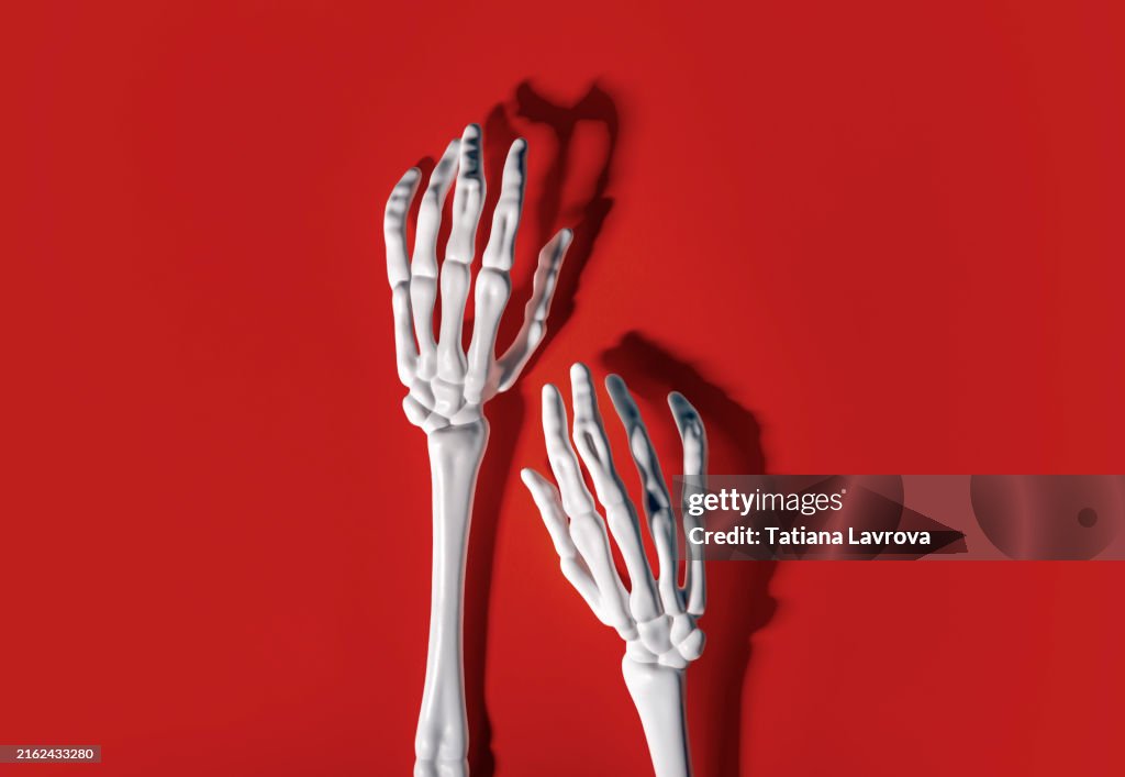 Two skeleton hands on vibrant red backdrop . Festive Halloween background with copy space
