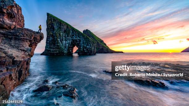 man looking at drangarnir natural arch at sunset - faroe islands stock pictures, royalty-free photos & images