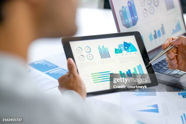 two business men meeting and looking at financial data, charts and graphs on a digital tablet and a laptop computer. - grafiek stockfoto's en -beelden