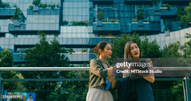 due giovani donne d'affari asiatiche che incontrano la discussione sulla strategia aziendale parlano al di fuori del moderno edificio per uffici. attività sostenibile all'aperto. - sostenibilità foto e immagini stock