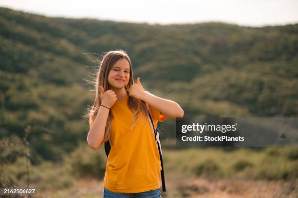 ritratto di ragazza con zaino e pollice in su in piedi su una montagna - una ragazza adolescente foto e immagini stock