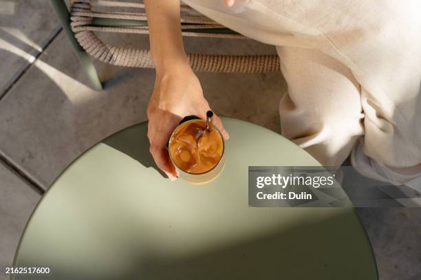 overhead view of a woman sitting in an outdoor cafe drinking an iced bumble coffee - iced coffee stock pictures, royalty-free photos & images