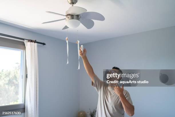 man turning on a ceiling fan with remote - ceiling fan stock pictures, royalty-free photos & images